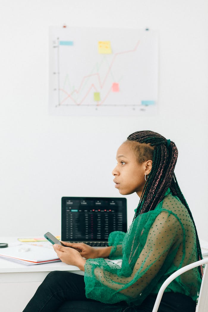 Focused woman in office analyzing financial graphs on laptop.