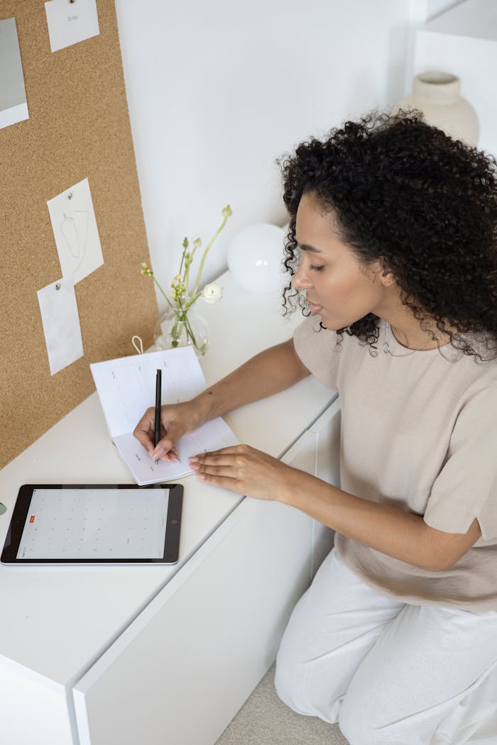 A young woman with curly hair writes notes in a modern office. Perfect for business planning concepts.